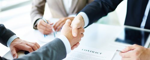 Making agreement Image of business partners handshaking over business objects on workplace