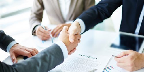 Making agreement Image of business partners handshaking over business objects on workplace